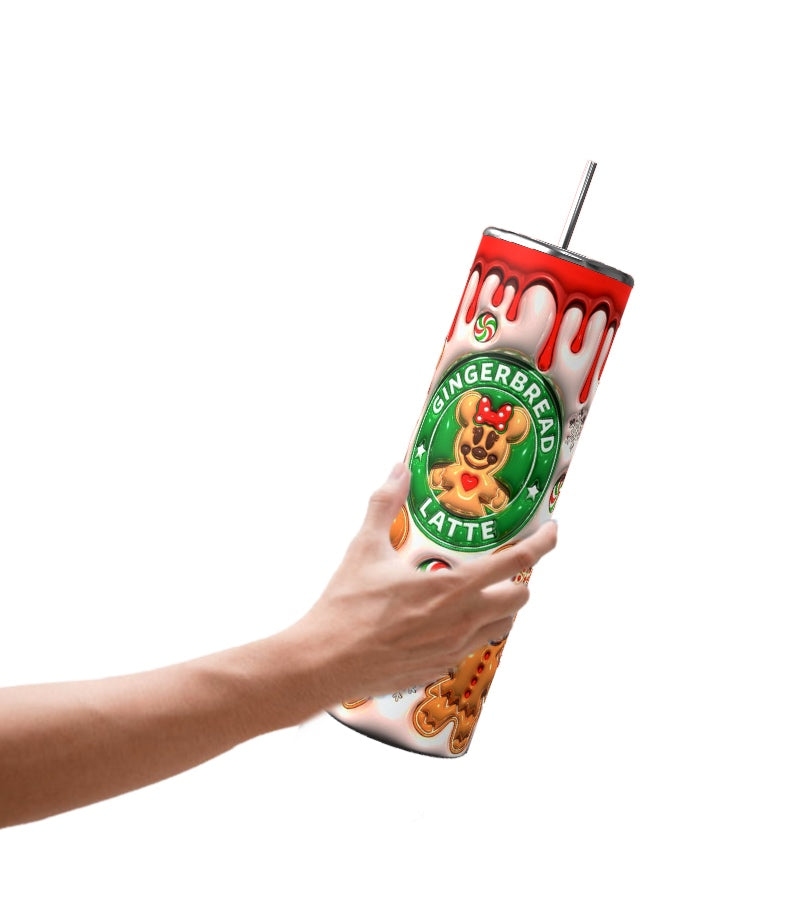 A hand holds a tall Gingerbread 20oz Tumbler by Kreative Kreationz, featuring a gingerbread latte design. The tumbler displays gingerbread men, a candy cane, and dripping icing details on the lid. A metal straw complements its durable construction, ensuring both style and functionality.