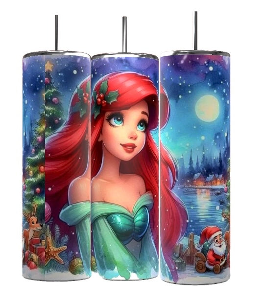 The Kreative Kreationz Princess Ariel 20oz Tumbler showcases three beautiful tumblers adorned with an illustrated design of a red-haired mermaid among cheerful holiday scenes, including a Christmas tree and snowman. The tumblers' backdrop is a snowy village beneath a moonlit sky, all finished with a practical spill-proof lid.