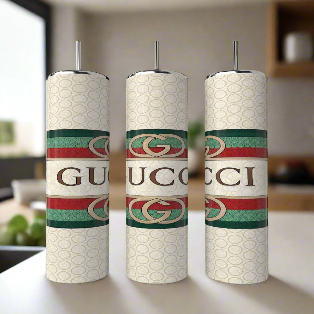 A set of three 20oz Gucci tumblers by Kreative Kreationz, each crafted from eco-friendly reusable materials, showcase a patterned design with bold logos and horizontal green and red stripes featuring the interlocking "G" emblem. These luxury items are set against a bright, modern kitchen backdrop.