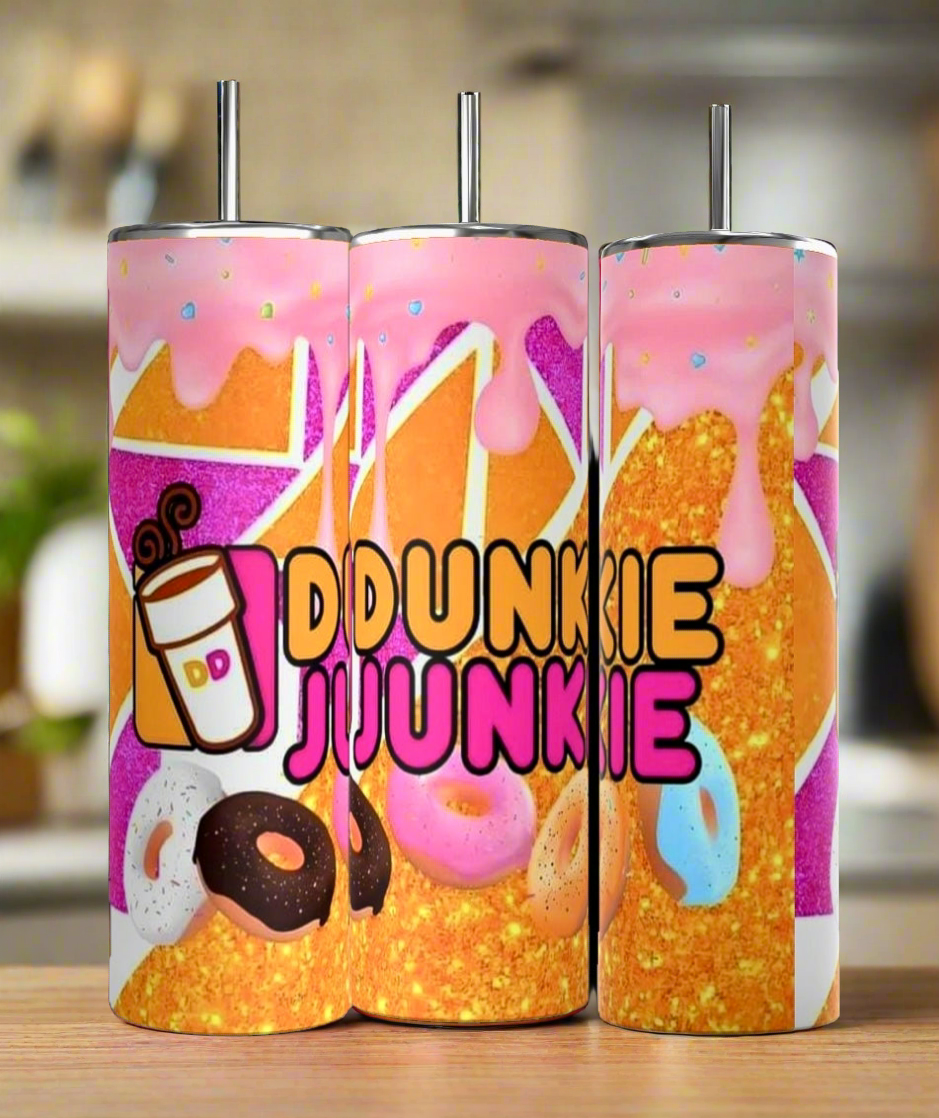 These Dunkin Junkie Drip 20oz Tumblers by Kreative Kreationz are vibrantly handmade and adorned with donut images and dripping pink frosting. The phrase "DUNKIN JUNKIE DRIP," accompanied by a small coffee cup icon on the left, is boldly printed on the front. They feature a glittery gold background.



