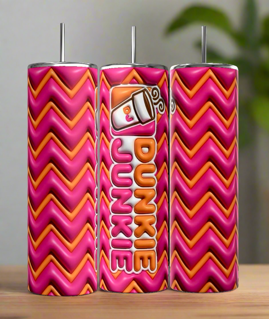 Three Kreative Kreationz Dunkin Junkie 20oz Tumblers, in pink and orange zigzag, stand on wood. The middle tumbler displays a coffee cup graphic with "Dunkie Junkie" text. Each comes with a reusable straw and holds 20 oz of your favorite drinks.