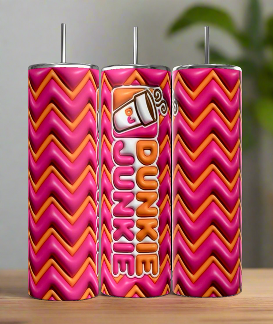 Three Kreative Kreationz Dunkin Junkie 20oz Tumblers, in pink and orange zigzag, stand on wood. The middle tumbler displays a coffee cup graphic with 