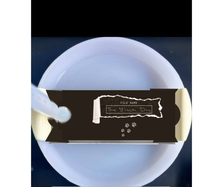 A white mug with a light blue handle is shown against a plain background. On top of the Kreative Kreationz Black Dog lid Plate/Topper, which fits 20, 30, and 40 oz Stanley cups, is a partially unwrapped chocolate bar with a black wrapper.