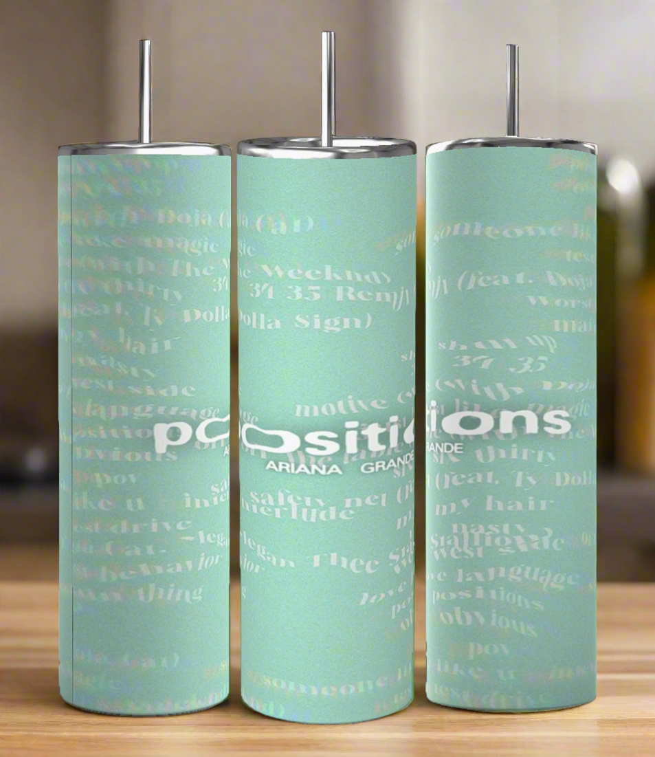 Three Positions Ariana Grande 20 oz skinny tumblers by Kreative Kreationz, featuring metal lids and straws, showcase a light green background adorned with white text and graphics. These eco-friendly cylinders, each displaying "positions," rest elegantly on a wooden surface.