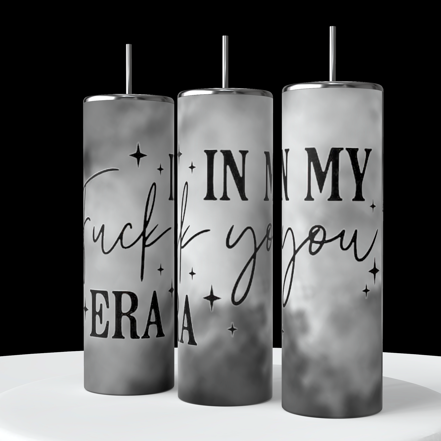 Three tall, cylindrical "In My Fuck You Era 20oz Tumblers" by Kreative Kreationz are displayed. Each tumbler features spill-proof lids and reusable black straws, with a gray and white gradient background. Bold text reading "Fuck you, I'm in my era" is prominently displayed, surrounded by small scattered stars.