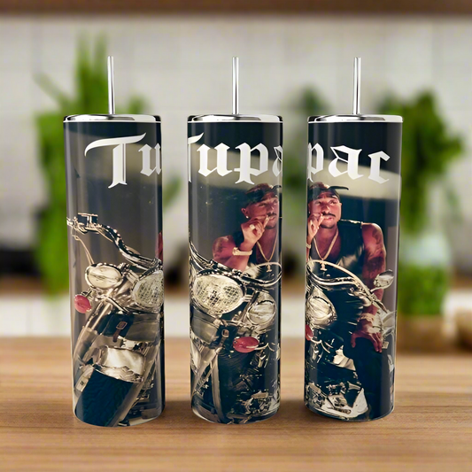 Three 20oz stainless steel tumblers from Kreative Kreationz stand on a wooden surface, each featuring a man in a bandana on a motorcycle with "Tupac" inscribed in white. They channel 2Pac's spirit against green foliage for an iconic vibe.