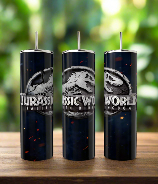 Three dark, glossy Kreative Kreationz 20oz tumblers with silver lids and straws feature the "Jurassic World: Fallen Kingdom" dinosaur skeleton logo. These eco-friendly items rest on wood against a backdrop of blurred green foliage.