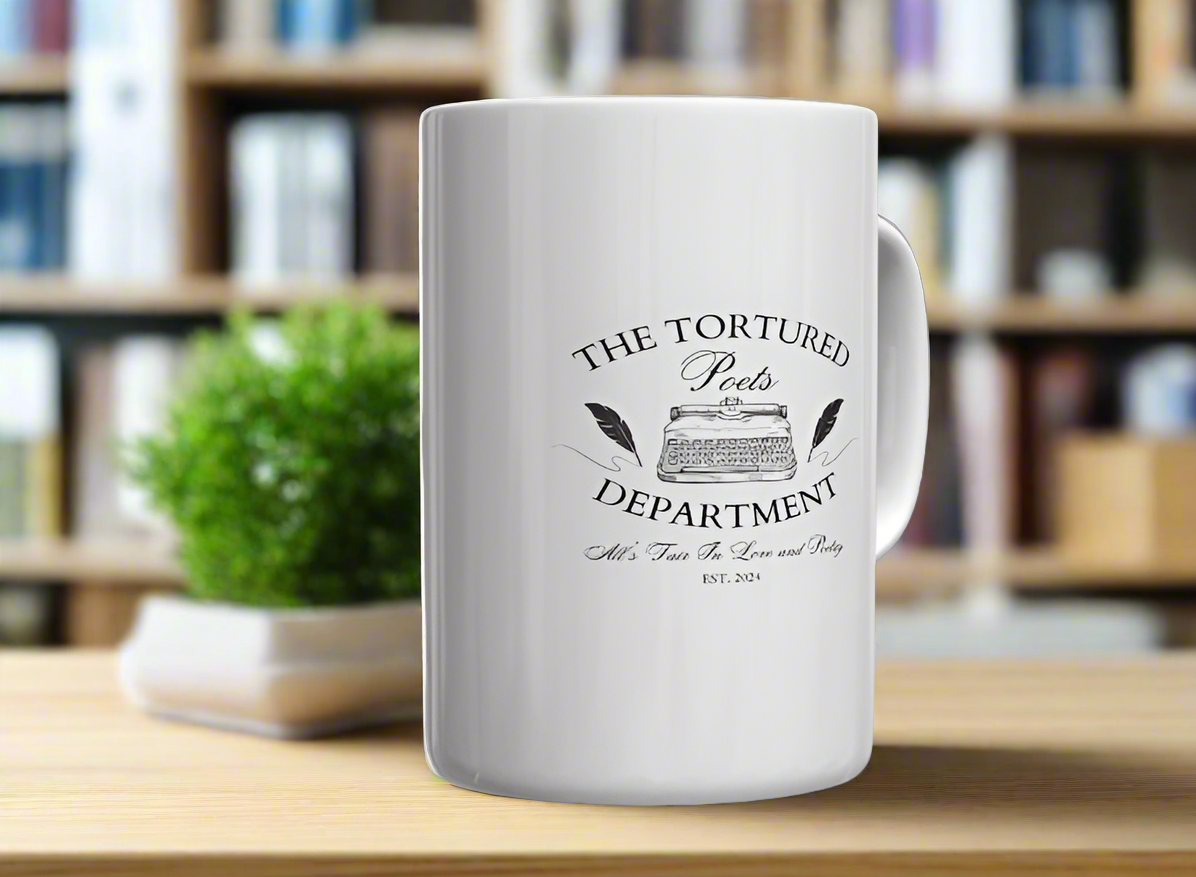 A white ceramic mug from Kreative Kreationz, named "The Tortured Poets Department | TTPD Ceramic Mug," features the text "The Tortured Poets Department" and an illustration of a vintage typewriter in the center. Below the illustration, it reads "All's Fair in Love and Poetry" and "Est. 2024." The mug is placed on a wooden surface with a plant in the background, making it perfect for any Taylor Swift fan.