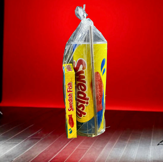 A plastic bag containing a Swedish Fish Gift Set with a 20oz stainless steel skinny tumbler, featuring yellow and blue packaging, branded 