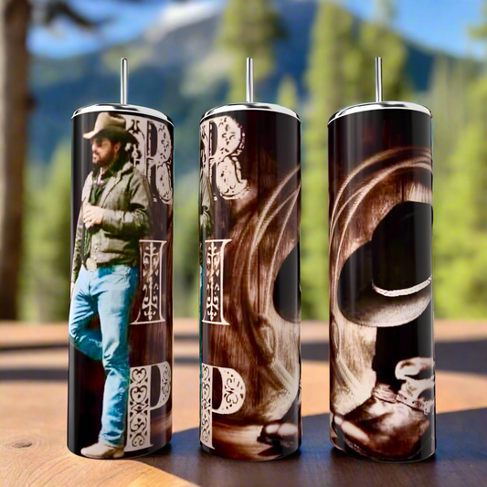 Three Kreative Kreationz Yellowstone RIP 20oz stainless steel tumblers with western-themed designs, featuring a cowboy and intricate lettering, stand proudly on a wooden surface against a blurred backdrop of forest and mountain.