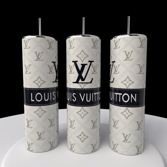 Three LV 20oz Skinny Tumblers by Kreative Kreationz are showcased on a white surface. These cylindrical tumblers feature spill-proof lids and display the LV logo with the name in a classic beige and white design, boasting a sleek 20 oz capacity.