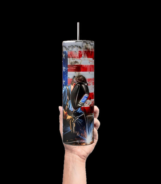 A hand holds the Welders 20oz Tumbler by Kreative Kreationz, featuring an American flag and a welder in a mask with sparks flying. This striking tumbler shines against a solid black backdrop.