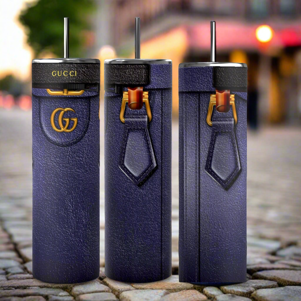 Three tall, cylindrical Gucci Diana-inspired purple tumblers from Kreative Kreationz, featuring a leather-like texture, gold Gucci logos, and black straws, stand on a cobblestone street. With durable construction and a 20 oz capacity, the focus remains on these stylish and luxurious cups against the softly blurred background.