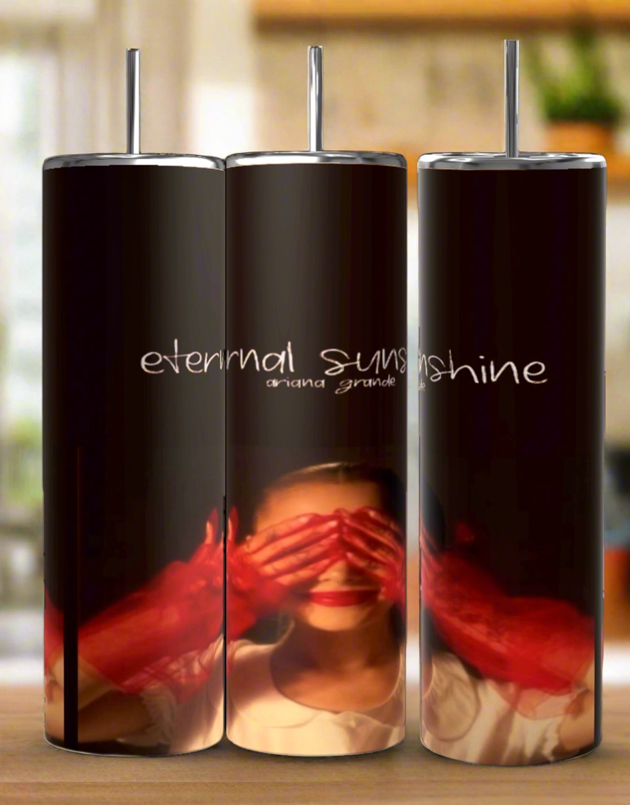 Kreative Kreationz offers three Ariana Grande External Sunshine 20oz Tumblers, each with a spill-proof lid and featuring a design of a woman covering her eyes while "eternal sunshine" floats above. The dark background beautifully integrates with a blurred, warm-toned image to create an intriguing visual effect.