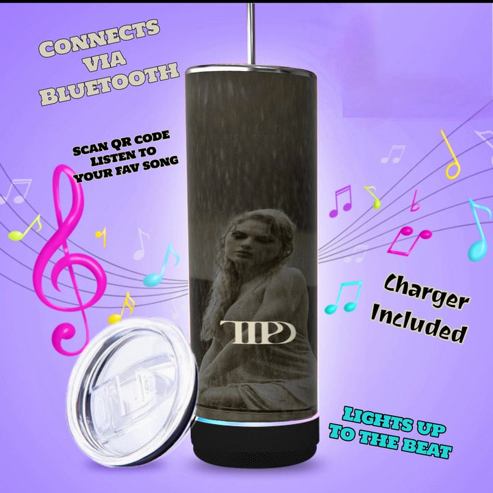 Three TTPD Bluetooth Tumblers by Kreative Kreationz, featuring a black cylindrical design with pink bases, are displayed. Each tumbler showcases a statue motif and the initials "MP." On the left, a smartphone screen displays a music app. A USB charging cable and a lid are placed beside the tumblers, with musical notes in the background.