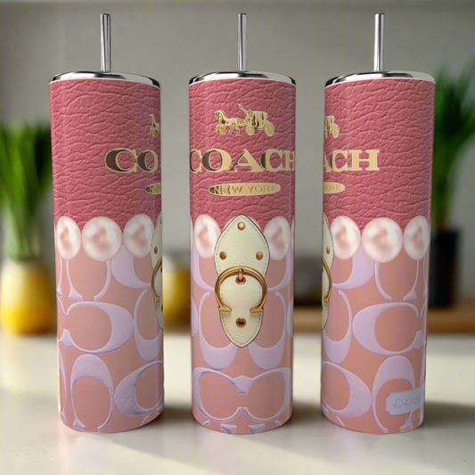 Three pink Kreative Kreationz Coach 20oz Skinny Tumblers, complete with metal straws, feature the luxury-inspired Coach logo, a gold horse and carriage motif, and intricate patterns on the counter, while kitchen items appear blurred in the background.