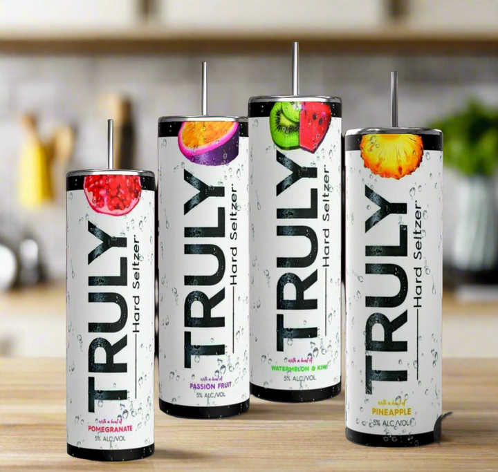 Four cans from the Truly Hard Seltzer 20oz Skinny Tumbler Collection by Kreative Kreationz are displayed on a wooden surface. The flavors showcased are pomegranate, passion fruit, pineapple, and another indistinguishable fruit. The sleek, tall cans feature refreshing water droplets on their design. Enhance your drinking experience with a reusable straw for an eco-friendly touch.