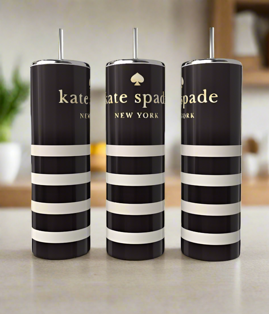 Three Kate Spade 20oz Skinny Tumblers from Kreative Kreationz, featuring black and white stripes with silver lids and straws, sit elegantly on a countertop. The blurred kitchen background, with plants and shelves, enhances the drinkware's allure.