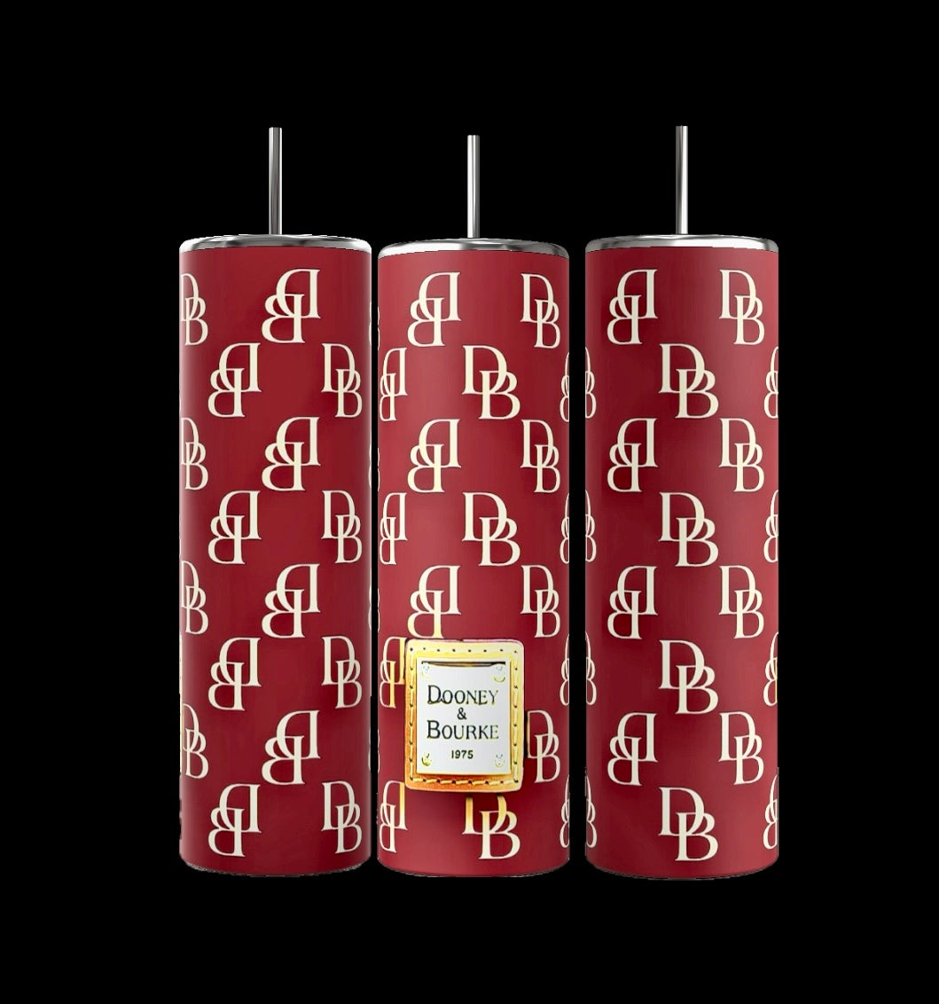 The D&B 20oz Tumbler set from Kreative Kreationz includes three tall, cylindrical tumblers adorned with burgundy and white "DB" patterns in a sleek, modern sublimate style. Each tumbler is equipped with a metal straw, and the central piece is labeled "Dooney & Bourke 1975," showcasing their chic craftsmanship.