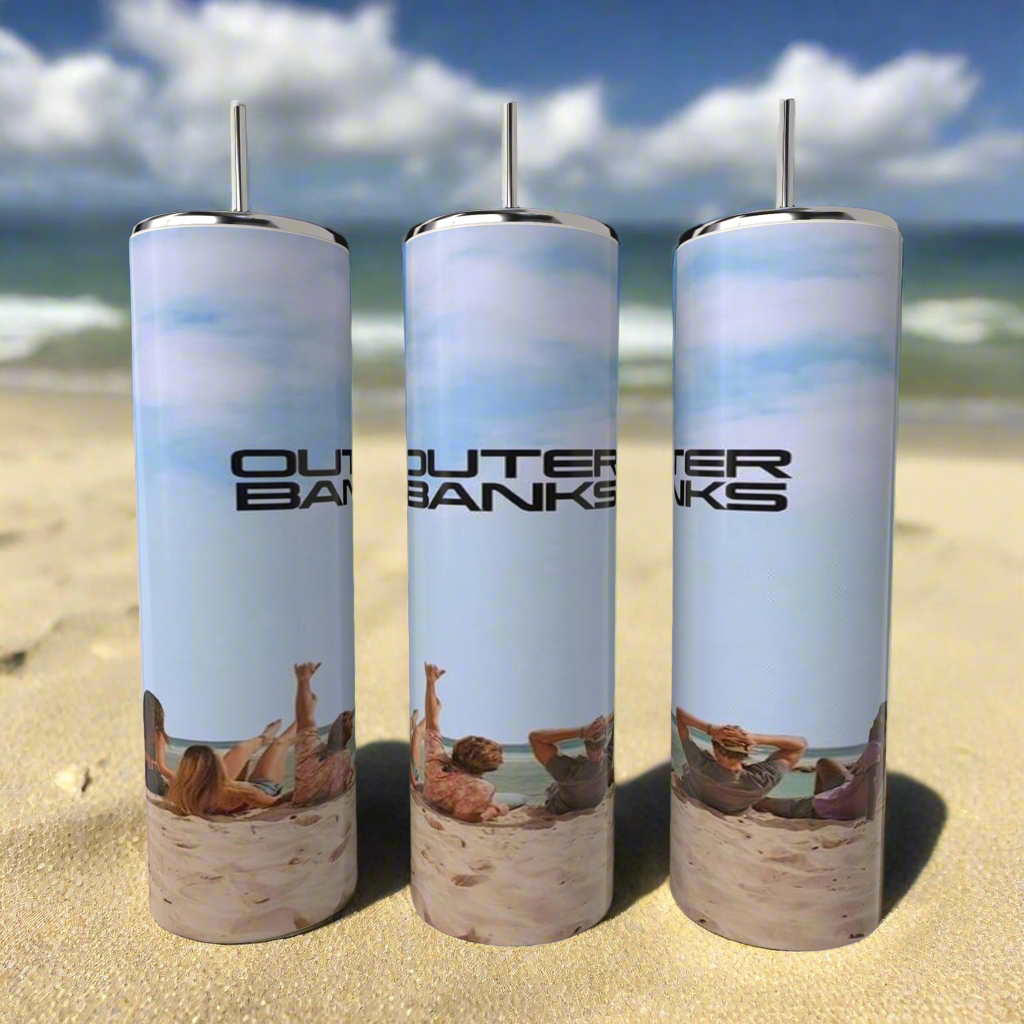 Three Outer Banks OBX 20oz Tumblers by Kreative Kreationz sit on a sandy beach, capturing the scene of beachgoers under a clear sky with ocean waves. Made of stainless steel, each tumbler is ideal for relaxing by the ocean.