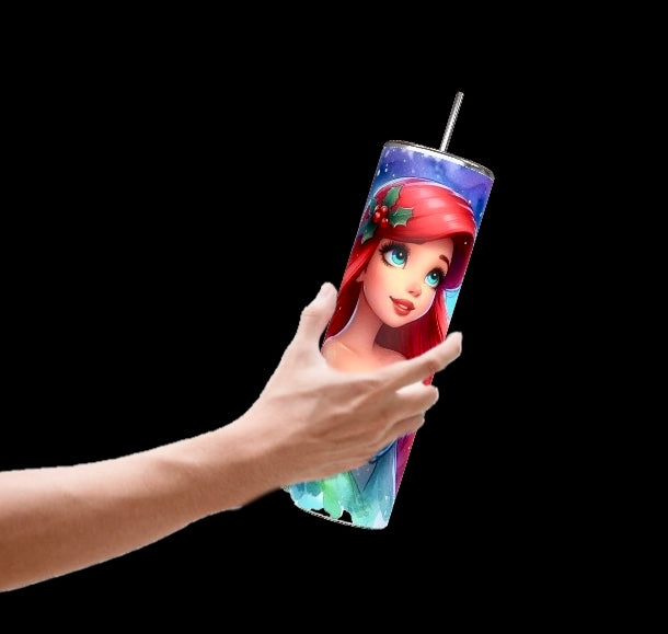 A hand holds the Princess Ariel 20oz Tumbler from Kreative Kreationz, featuring a vibrant depiction of Ariel with her long red hair against a colorful starry background set on black. This tumbler comes with a spill-proof lid, making it perfect for securing your drink while on the go.