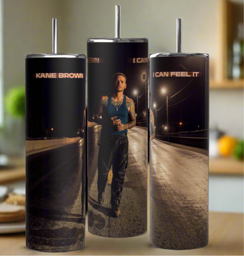 Three Kane Brown Miles On It 20oz Tumblers by Kreative Kreationz display a street scene with a dark-clad figure holding a drink. Featuring "KANE BROWN" and "I CAN FEEL IT" text, they are set against a softly lit luxury kitchen backdrop. Made of high-quality stainless steel, they're stylish and durable.