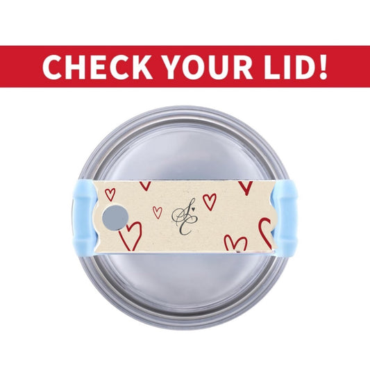 A silver tumbler filled with black liquid features a beige piece of tape adorned with red hearts and a cursive letter "E" on the lid. The tape covers the drinking hole while a clear straw is inserted into another hole, giving it the appearance of being topped with Kreative Kreationz's Sabrina Carpenter Heart Stanley Lid Plate/Topper.