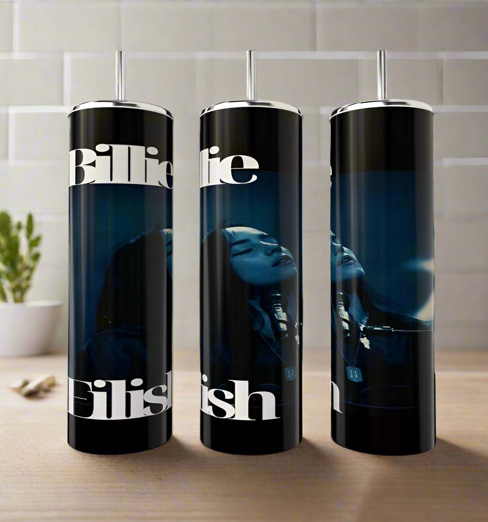 Three Billie Eilish Tumblers by Kreative Kreationz display an artistic image of a singer with "Billie" and "Eilish" adorned in elegant print. These black, cylindrical tumblers exude luxury resting on a white surface in a tiled room, enhanced by the presence of a small plant.