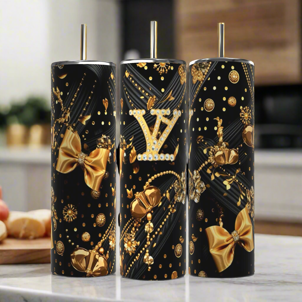 Three stylish, cylindrical Kreative Kreationz tumblers in a black finish feature golden bows and pearls, each displaying the iconic "LV" logo. The design of the Louis Vuitton Black & Gold 20oz Tumbler includes elaborate gold and pearl patterns set against a blurred kitchen background.