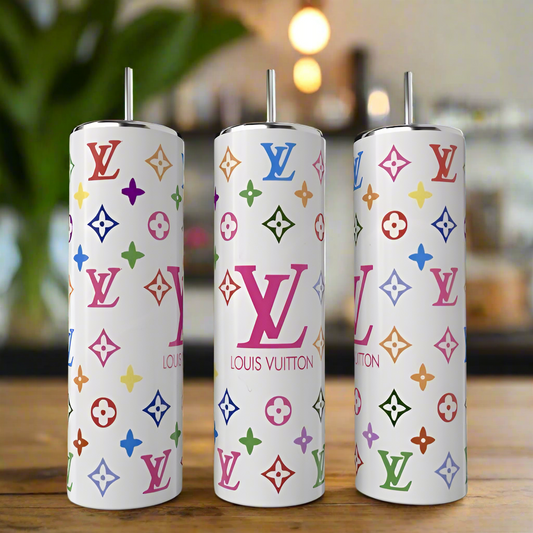 Three sleek, white Louis V Multicolor tumblers by Kreative Kreationz, each 20oz with colorful logos, rest on a wooden table. The stainless steel finish offers a luxury-inspired design against a blurred background that suggests a cozy setting with green foliage.