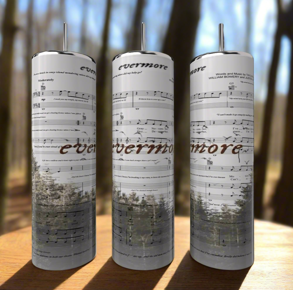 The Evermore | Taylor Swift 20oz Skinny Tumbler by Kreative Kreationz showcases musical sheets and "evermore" text against a blurred forest backdrop, complete with tall trees. Featuring a reusable straw and spill-proof lid, this tumbler effortlessly combines style with functionality.