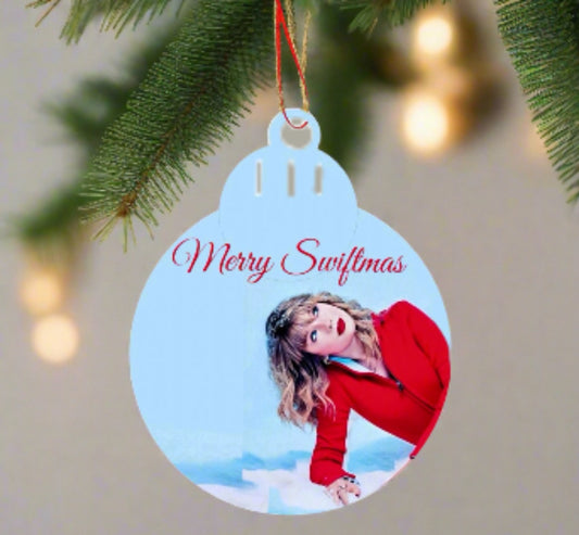 A festive decorator's delight, the Merry Swiftmas Tree Ornament by Kreative Kreationz features a woman in red against a blue background. "Merry Swiftmas" is written in elegant red cursive, complemented by softly twinkling warm lights.