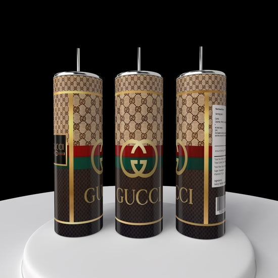 On a white surface, three Gucci 20oz Skinny Tumblers from Kreative Kreationz are showcased, featuring double-wall insulation and the iconic Gucci logo with a gold, green, and red pattern. The cylindrical tumblers with straws appear in various angles against a black background.