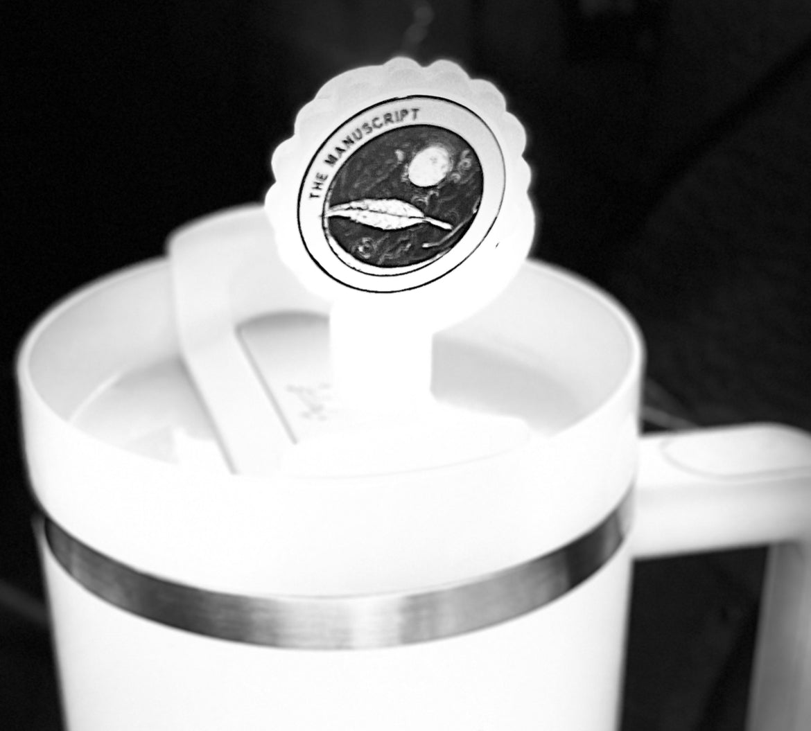 A white cup with a handle displays a round sticker on the lid, which features an illustration of a planet and spacecraft, accompanied by the text "THE MANUSCRIPT" around it. The background is black and the image appears in black and white. For added convenience, it pairs well with Kreative Kreationz's Straw Cover Topper, which fits Stanley cup sizes 40oz, 30oz, and 20oz with 10mm straws.