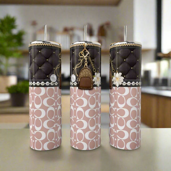 Three elegant Coach Lil Backpack 20oz Tumblers by Kreative Kreationz sit on the countertop. Each has a quilted black top and charming accent, with pink lower halves featuring white abstract designs, all made from eco-friendly, reusable materials against a blurred kitchen backdrop.