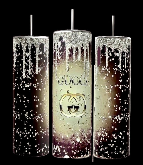 A set of three tall tumblers, each adorned with metallic straws, displays a white speckled pattern reminiscent of splattered paint. The central tumbler, identified as the Gucci Drop 20oz Tumbler by Kreative Kreationz, prominently showcases the iconic logo against a black background. Their durable construction enhances the striking contrast of the design.