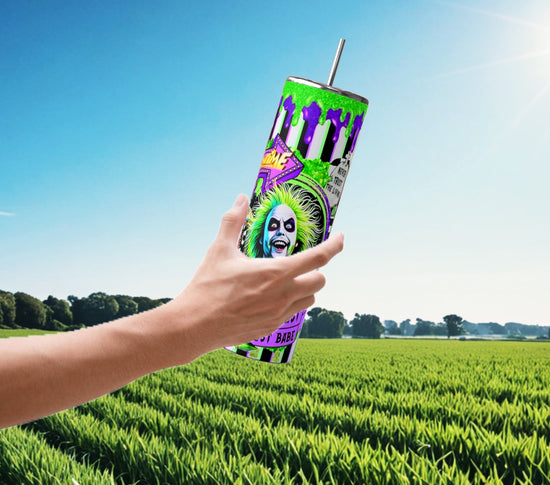 A hand holds a vibrant Beetlejuice Striped 20oz Tumbler by Kreative Kreationz, showcasing bold, bright colors and a cartoonish face with green hair set against a lush field. This Halloween drinkware comes with a straw for convenient sipping on the go.