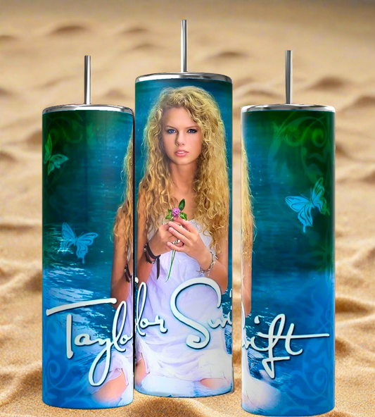 The Debut Taylor Swift 20oz Tumblers by Kreative Kreationz feature a person with long curly hair holding a pink rose against a blue-green butterfly background. The luxury-inspired design includes a stylized signature, set on sandy backdrop, and comes with reusable straws.