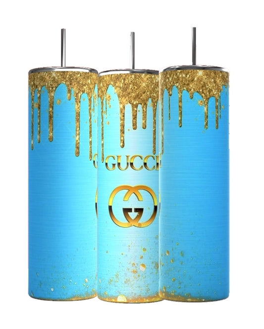 The Kreative Kreationz Gucci Blue Drip 20oz Tumbler features a striking blue base with gold paint drips, resembling GUCCI's style. It bears a central gold logo and includes a spill-proof lid with an inserted metal straw for convenience.