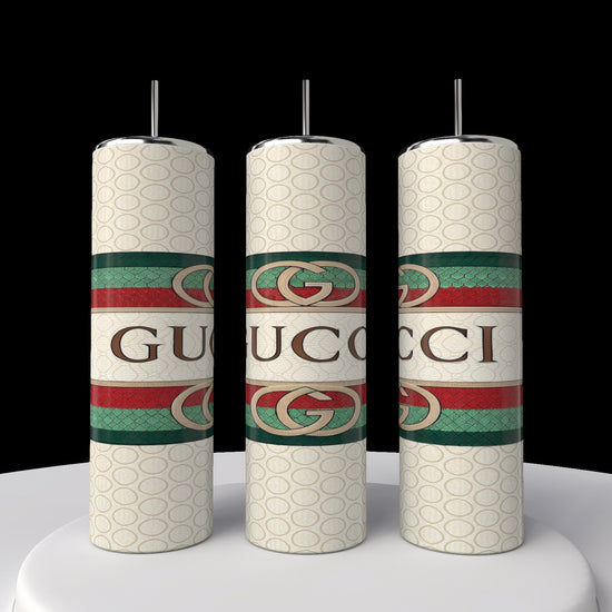 Three white candles with the Gucci logo stand on a white surface against a black background. Each displays the iconic green and red stripes, reflecting the design of Kreative Kreationz's new Gucci 20oz Tumbler collection.