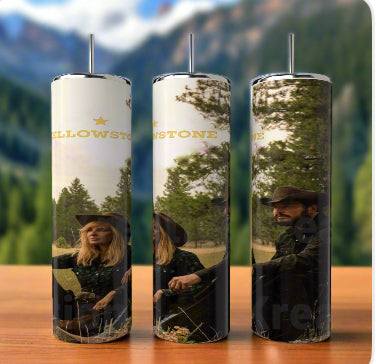 Displayed on a wooden surface, three Yellowstone 20oz Tumblers by Kreative Kreationz feature a design of a couple in cowboy hats amidst trees and mountains, with "Yellowstone" elegantly incorporated, capturing an adventurous spirit.