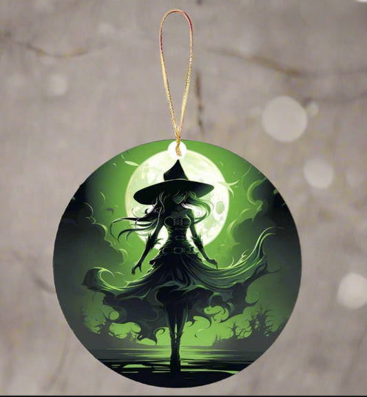 The Wicked Witch Christmas Tree Ornament by Kreative Kreationz is a round ornament showcasing the silhouette of a hat-wearing witch against a luminous green full moon. Her flowing cloak creates an enchanting effect with swirling wisps of smoke or magic. This wicked ornament features a sublimated design and includes a gold string for easy hanging.