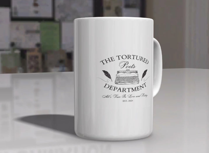 A white ceramic mug from Kreative Kreationz, named "The Tortured Poets Department | TTPD Ceramic Mug," features the text "The Tortured Poets Department" and an illustration of a vintage typewriter in the center. Below the illustration, it reads "All's Fair in Love and Poetry" and "Est. 2024." The mug is placed on a wooden surface with a plant in the background, making it perfect for any Taylor Swift fan.