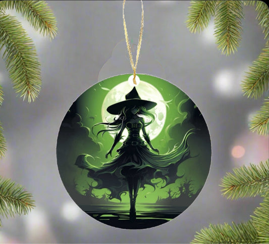 The Wicked Witch Christmas Tree Ornament from Kreative Kreationz dangles elegantly on the tree, featuring the silhouette of a witch with a flowing dress and hat set against a glowing green moon. This magical holiday decoration, nestled among evergreen branches, crafts a festive yet enchanting atmosphere.