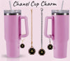 A pink tumbler with a straw and handle sits next to Kreative Kreationz's Chanel Charm Dangle, a custom cup accessory. Each charm features a circular 