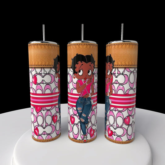 Three vibrant Kreative Kreationz Betty B Coach 20oz Skinny Tumblers, each adorned with Betty Boop in a pink shirt and ripped jeans against pink and white heart-striped patterns, are showcased with metal straws on a round white surface.