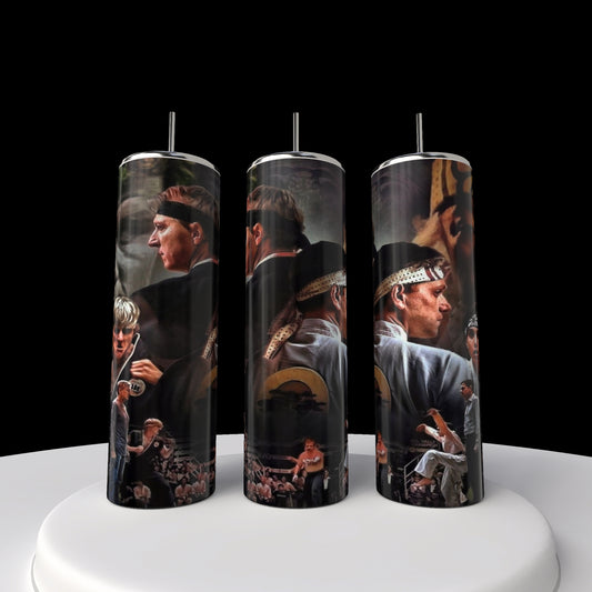 Three tall cylindrical candles echo the style of a Kobra Kai 20oz Stainless Steel Tumbler by Kreative Kreationz, featuring martial arts scenes with headband-wearing figures in karate poses. They stand on a round white platform set against a sleek black background.