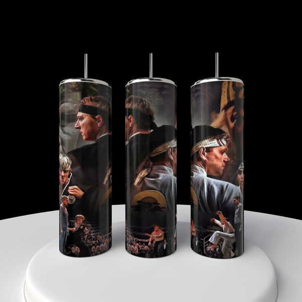 Three Kreative Kreationz Kobra Kai 20oz cylindrical stainless steel tumblers with martial arts scenes and characters in action poses. The imagery pops against a black background on a circular white platform, ideal for any Kobra Kai enthusiast.