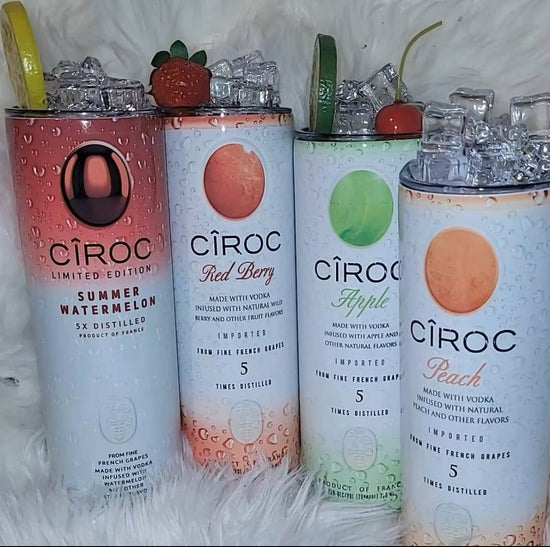 Two cans of Kreative Kreationz Ciroc 20oz Tumbler with 3D Lid Topper are shown on a wooden surface, reminiscent of travel tumblers. The left can is Red Berry flavor, topped with ice and a cherry. The right can is Vodka Snap Frost flavor, topped with ice and a lemon slice. Both cans feature product information and branding.